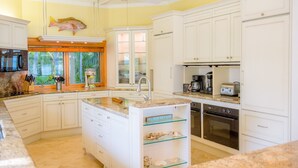 A modern kitchen with white cabinets, a granite countertop, a central island, a fish decoration on the wall, and a window with a view of greenery. - Island Palm Estate in Islamorada (Islamorada)