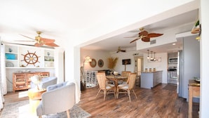 Amplia sala de estar con piso de madera, una mesa de comedor con sillas de mimbre y ventiladores de techo.