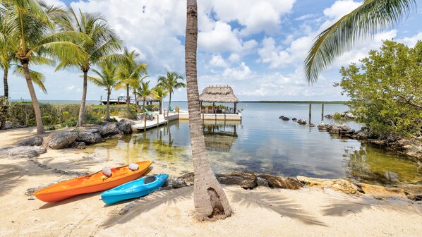 A beach with kayaks, a thatched-roof hut, and a calm sea.