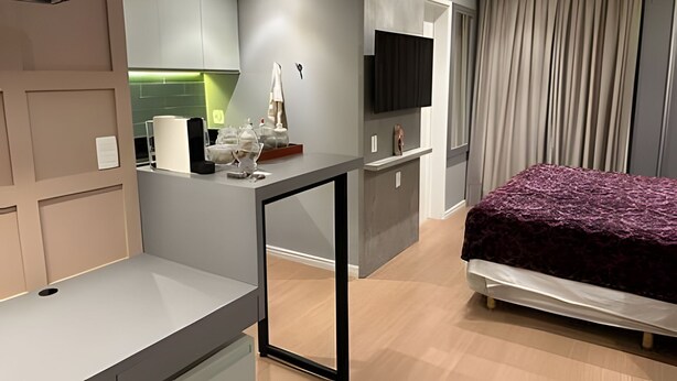 Una habitación de hotel moderna con cama, escritorio, televisor y kitchenette.