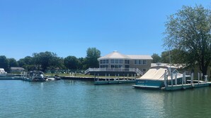 A marina with boats docked, a covered boat, and a building with a large window and balcony. - Charming 3-BR house w/golf, pool, WiFi, AC at pet friendly Middle Bass Island (Middle Bass)