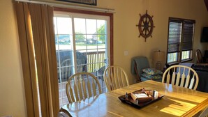 A dining area with a wooden table, chairs, a window with blinds, a wall-mounted ship's wheel, and a sign above the window. - Charming 3-BR house w/golf, pool, WiFi, AC at pet friendly Middle Bass Island (Middle Bass)