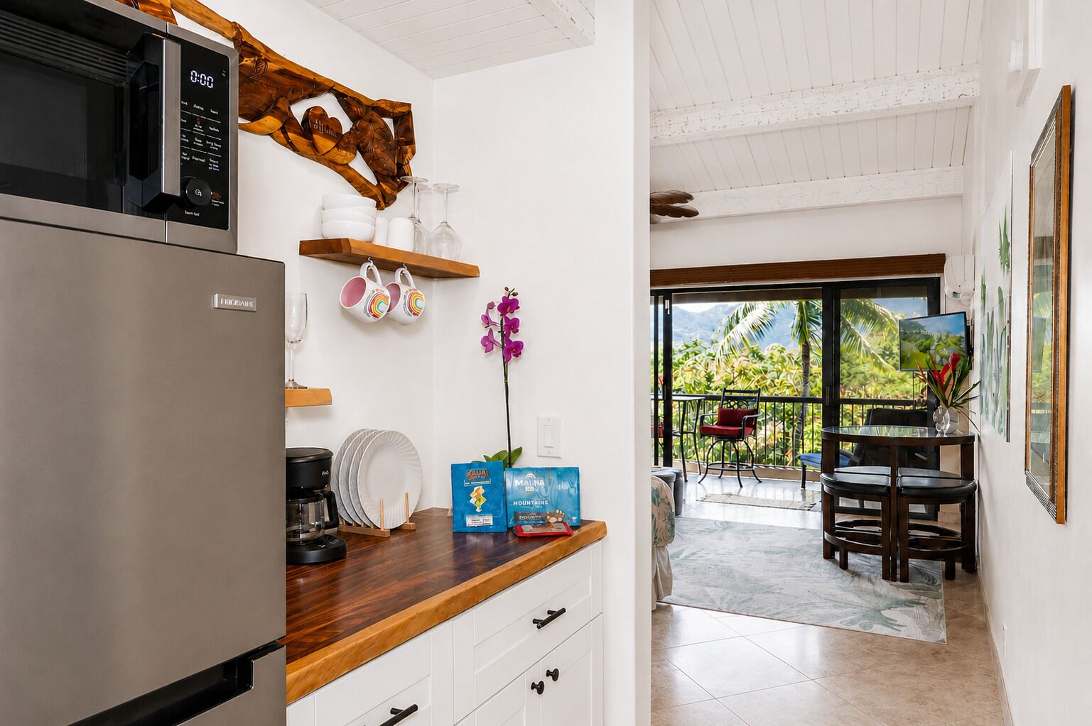 A kitchen with a refrigerator, microwave, and wooden countertop. There is a dining area with a table and chairs, and a view of the outdoors.