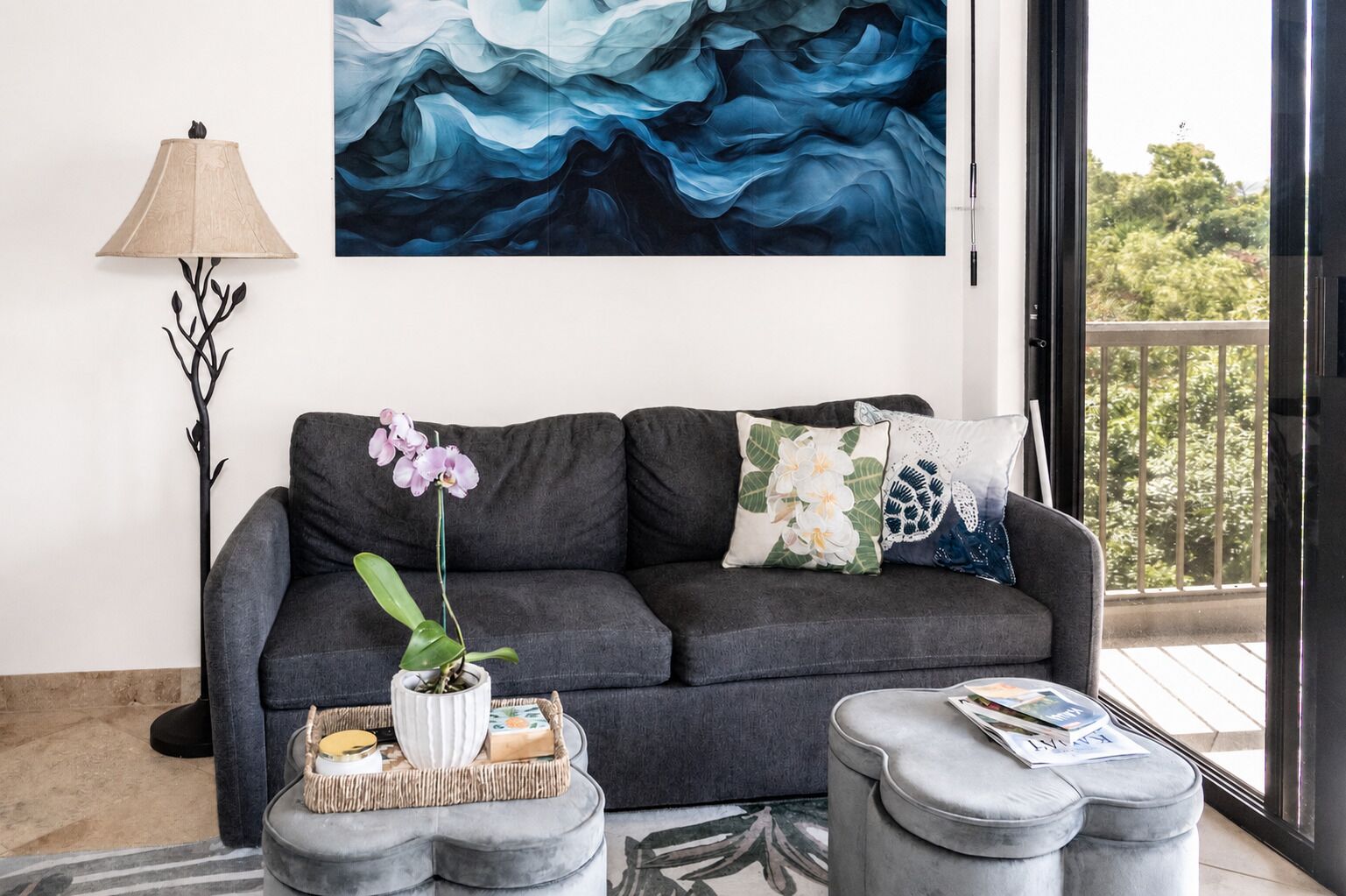 A modern living room with a grey sofa, decorative pillows, a vase with an orchid, a lamp, and a large abstract painting.