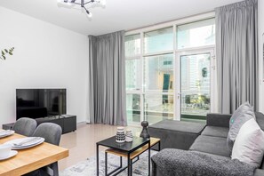 A modern living room with a flat-screen TV, a sofa, a dining table with plates and cutlery, and a small side table with decorative items.