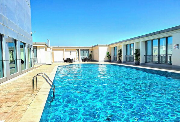 A swimming pool with a clear blue water surface, surrounded by a building with large windows and a tiled floor.