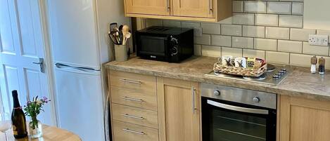 A compact kitchen with wooden cabinets, a built-in oven, a microwave, and a stainless steel range hood.
