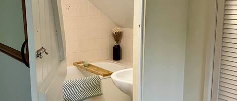 Un corridoio stretto che porta a un bagno con WC, lavandino e zona doccia.