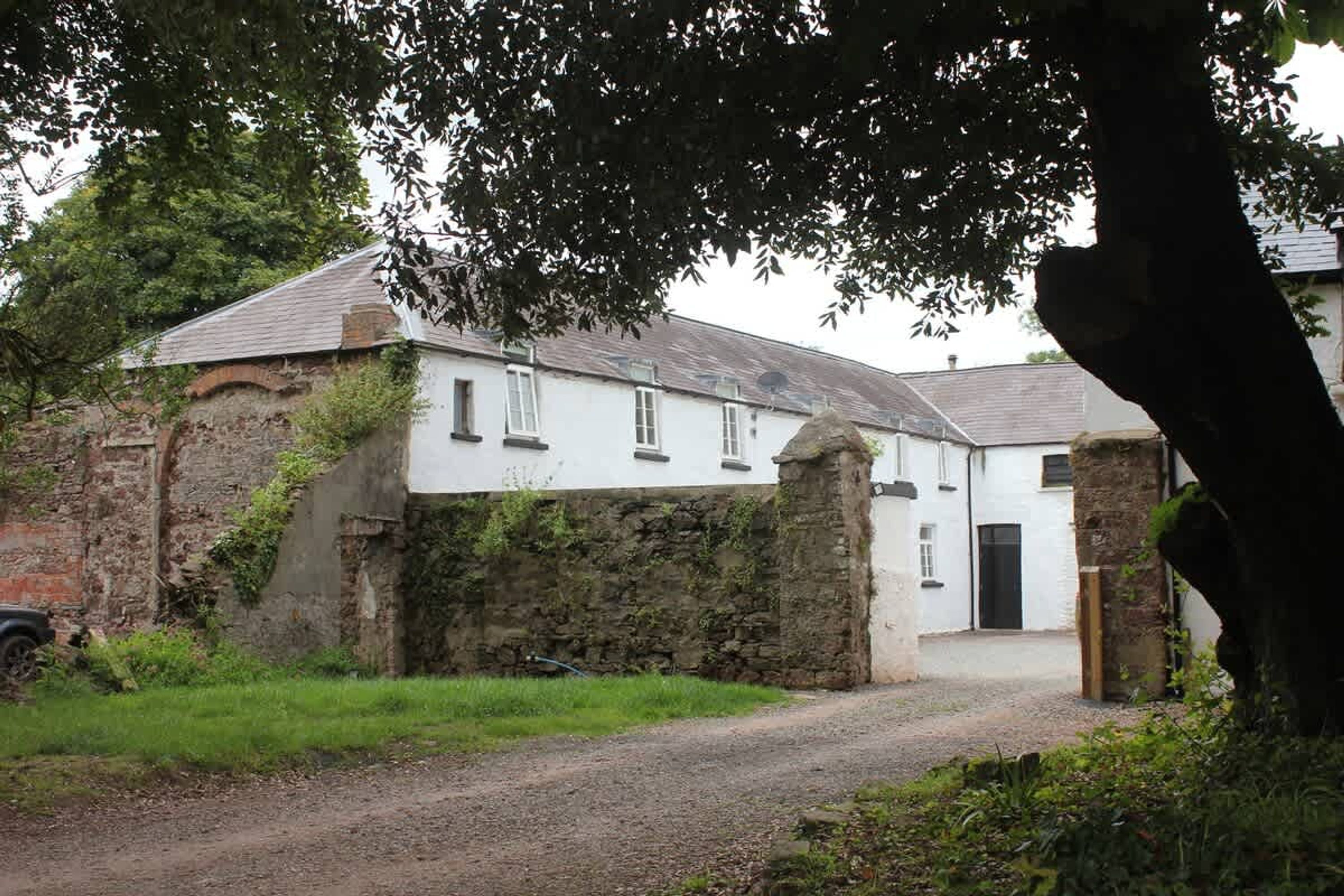 A white building with a stone wall and a gravel path leading to a black door.