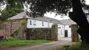 A white building with a stone wall and a gravel path leading to a black door.