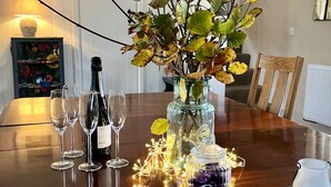 A dining table with a vase of autumn leaves, a bottle of wine, and a jar of berries. - Courtyard Cottage With hot tub and Walled Garden (Milford Haven)