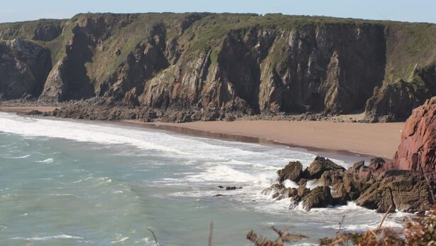 A coastal landscape with a beach, rocky cliffs, and ocean waves. - Courtyard Cottage With hot tub and Walled Garden (Milford Haven)