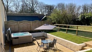 A patio with a hot tub, a table with chairs, and a grassy yard. - Courtyard Cottage With hot tub and Walled Garden (Milford Haven)