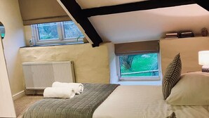 A bedroom with a sloped ceiling, a radiator, a window with a view of greenery, and a bed with a quilted bedspread and pillows. - Courtyard Cottage With hot tub and Walled Garden (Milford Haven)