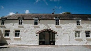 A white building with a symmetrical facade, multiple windows, and a central entrance with a decorative arch. - Courtyard Cottage With hot tub and Walled Garden (Milford Haven)