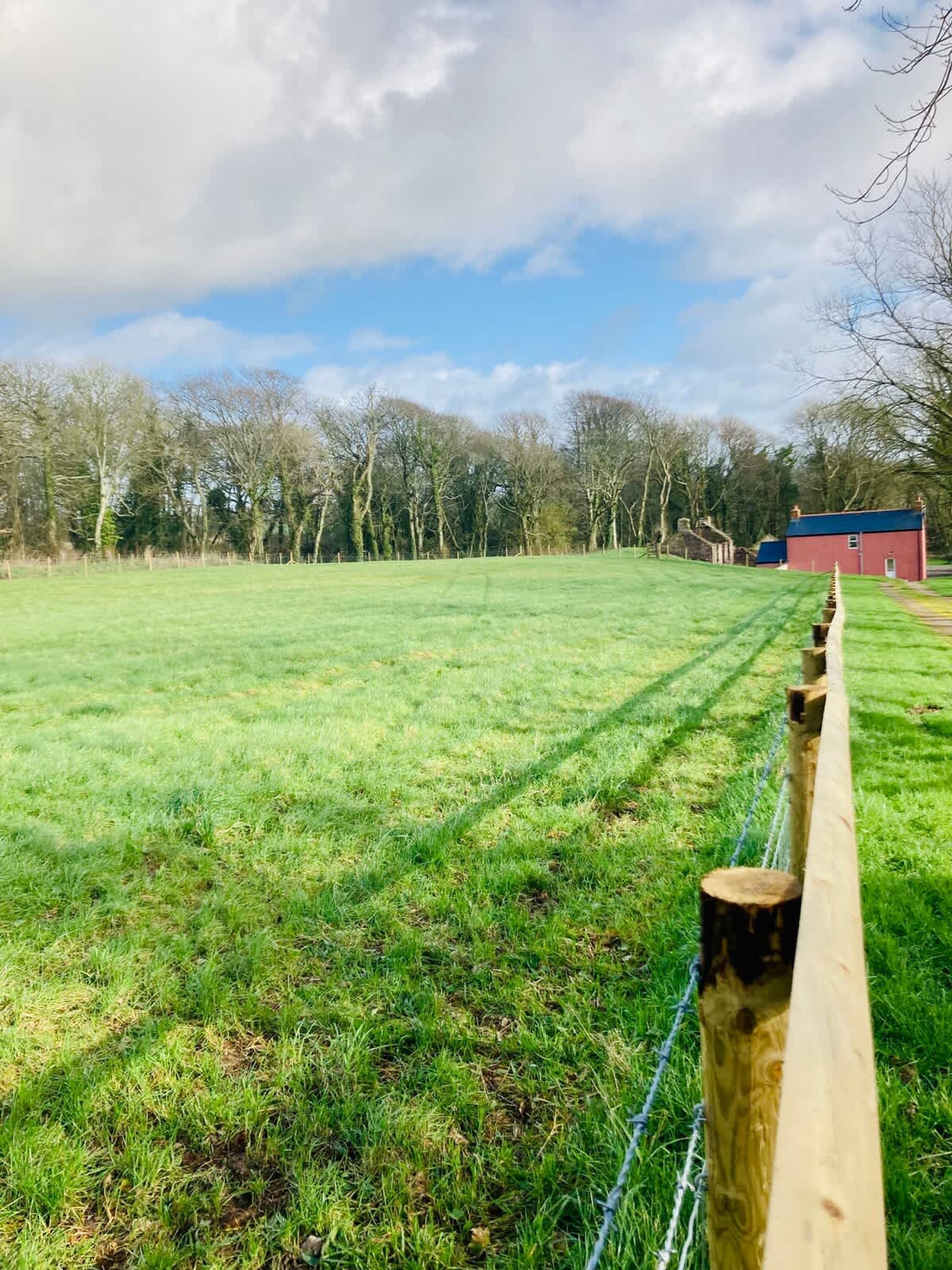 A grassy field with a wooden fence and a red building in the background.
