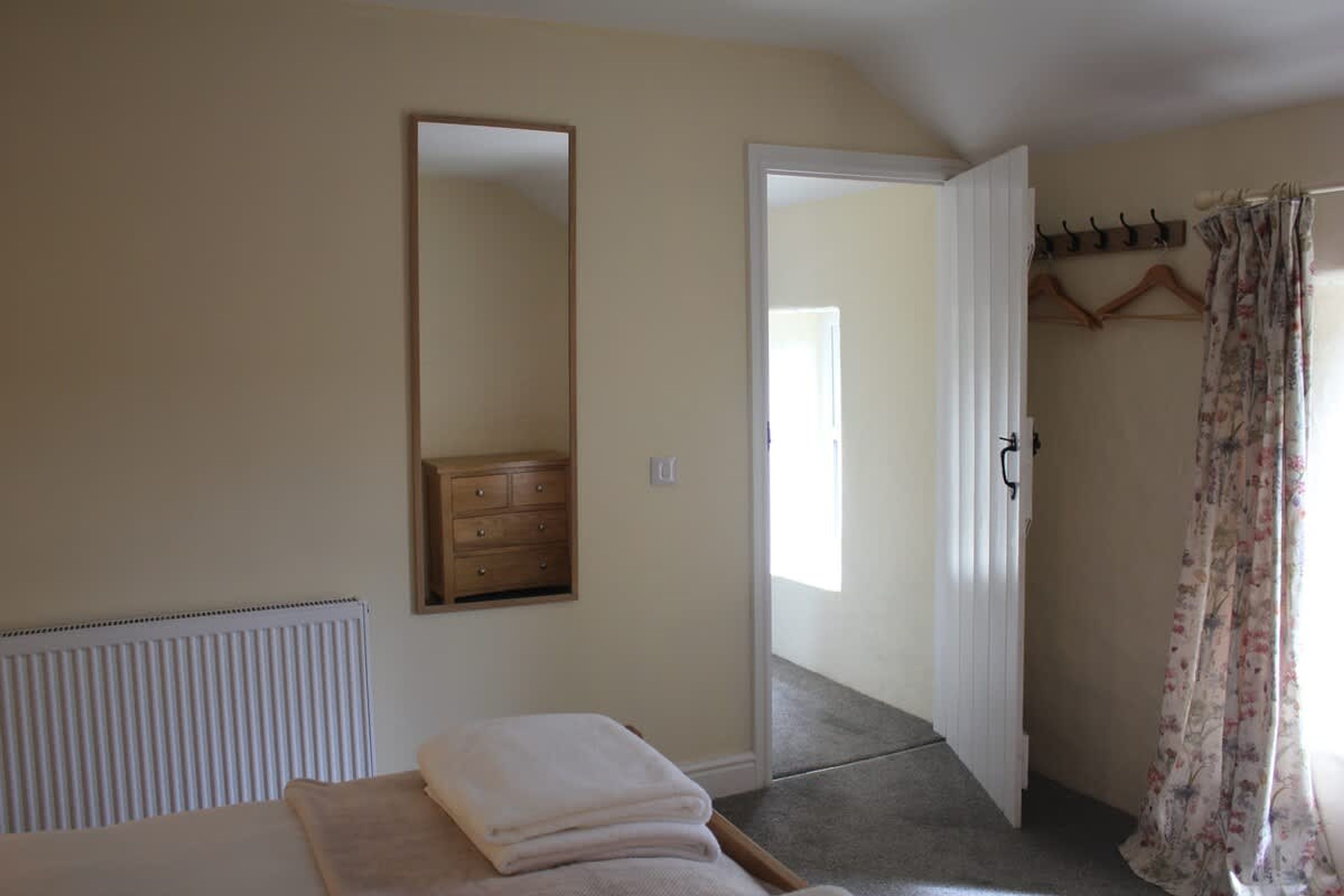 Un dormitorio con cama, cómoda, espejo, radiador y puerta que da a otra habitación.