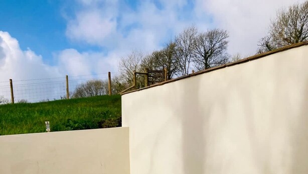 Un bain à remous doté d’un panneau de commande, entouré d’un mur blanc et d’une zone herbeuse.