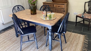 Un coin repas avec une table en bois, des chaises à revêtement noir, un vase de fleurs et une bibliothèque.