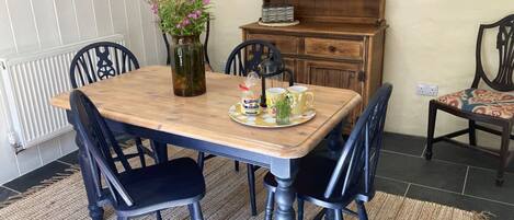 A dining area with a wooden table, black upholstered chairs, a vase with flowers, and a bookshelf.