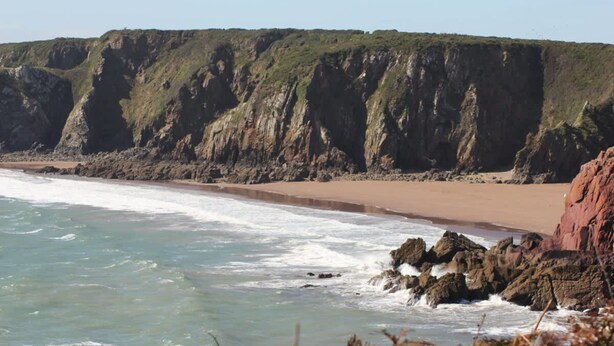 A coastal landscape with a beach, rocky cliffs, and waves crashing onto the shore.