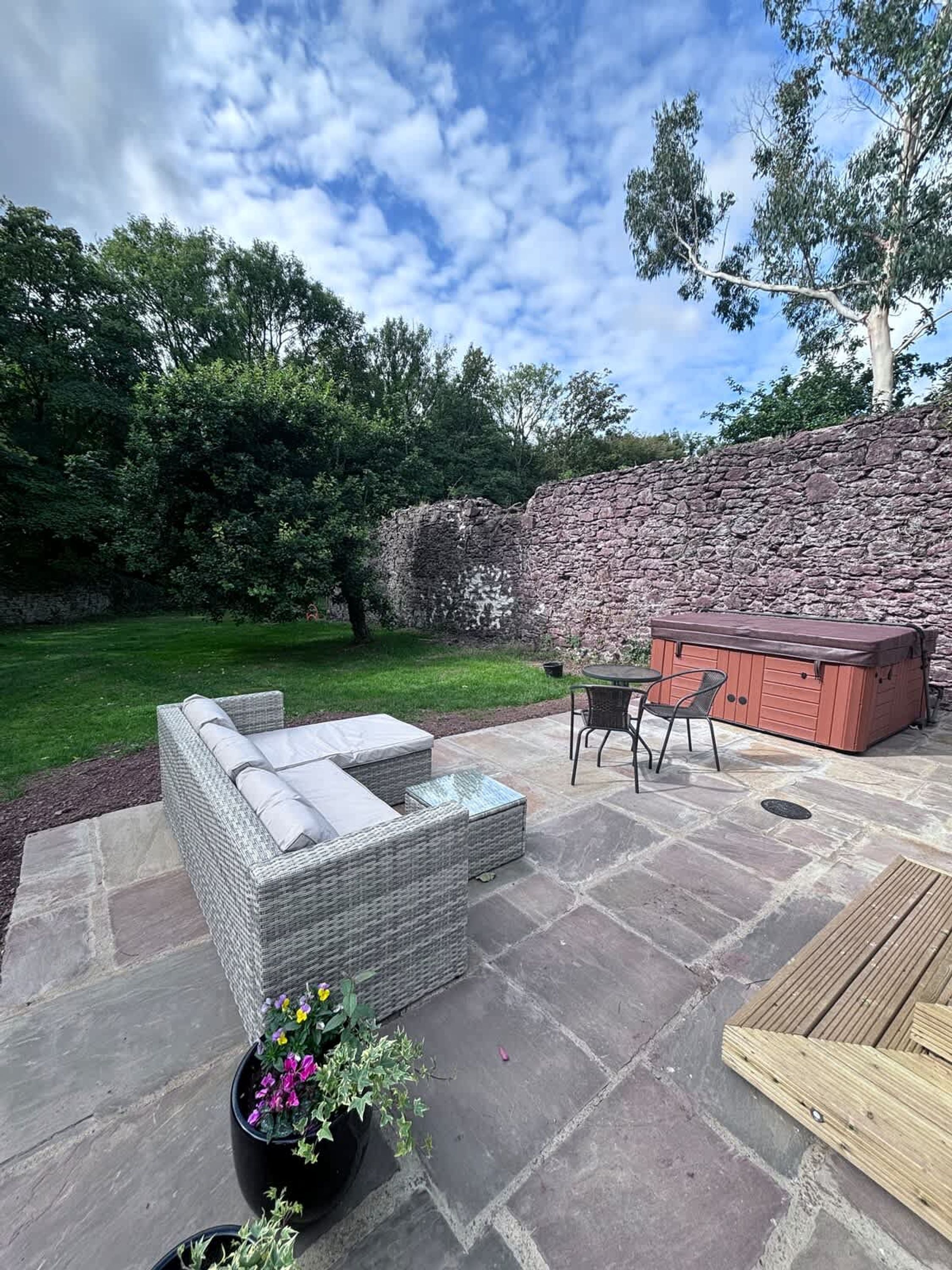Un patio con suelo de piedra, mobiliario de mimbre, jacuzzi y pared de piedra.