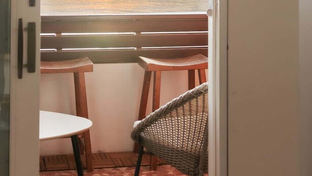 Un balcon avec vue sur le coucher de soleil sur l’océan, deux tables en bois et une chaise en osier.