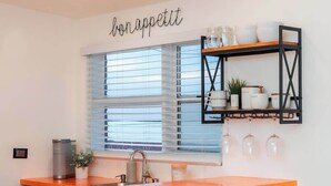 Une cuisine dotée d’un îlot central, d’un four encastré, d’un évier et d’une fenêtre avec des stores.