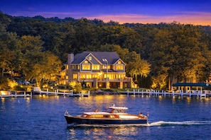 A large, two-story house with a dock and a boat in the foreground. - Geneva Lakefront Luxury Home with Private Pier Tennis Court (Lake Geneva)