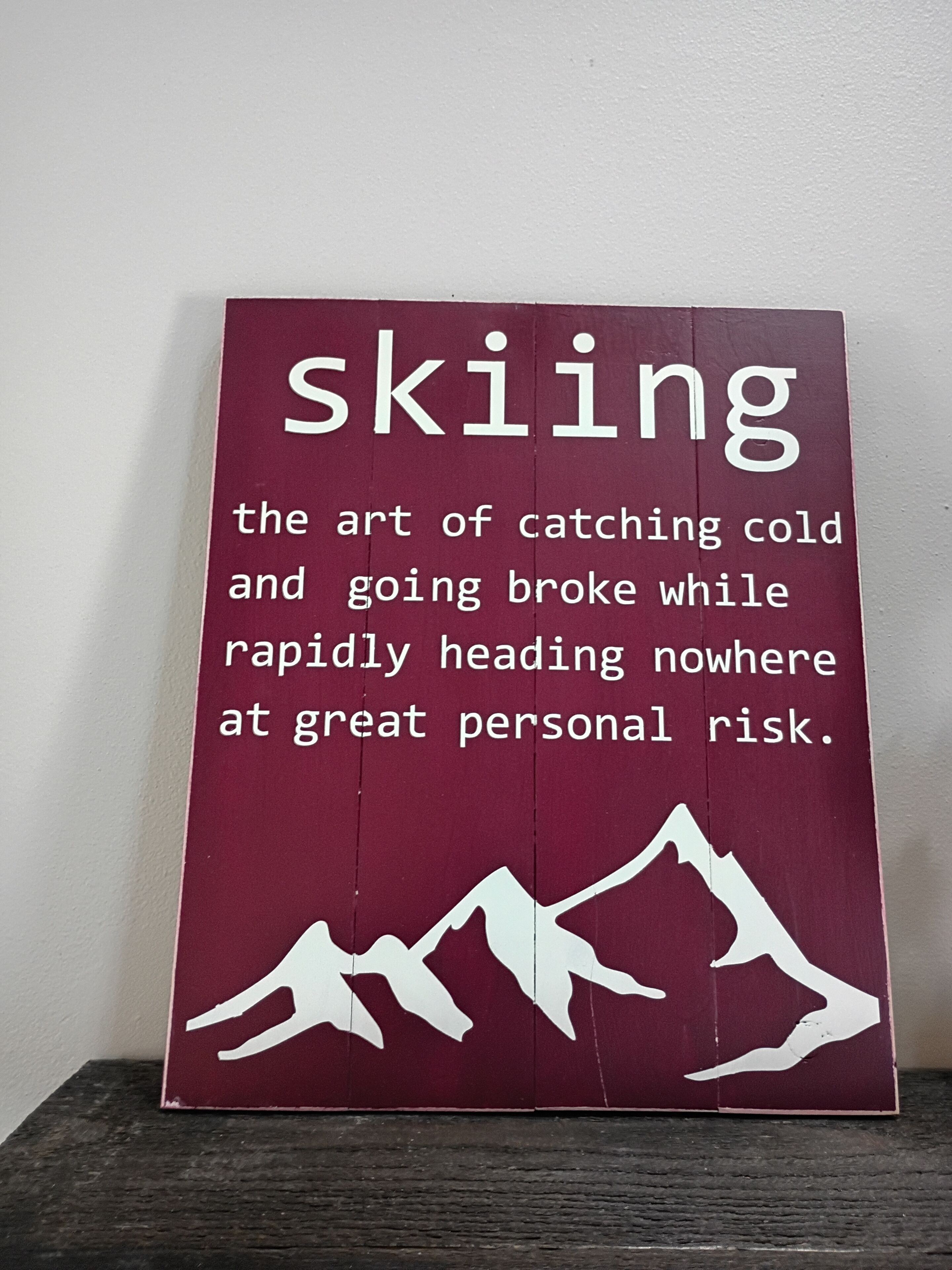 A maroon sign with white text and mountain silhouettes, defining skiing.