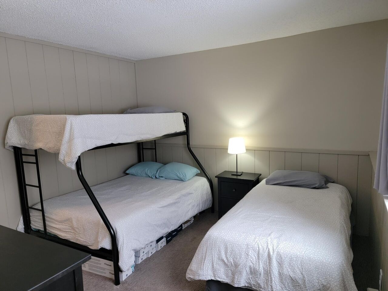 A room with bunk beds, a nightstand with a lamp, and a dresser.