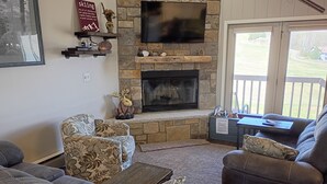 Una sala de estar con chimenea de piedra, televisor montado y vistas al exterior a través de una puerta corrediza de vidrio.