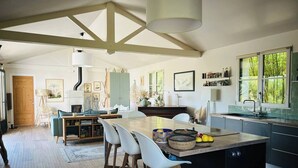 A modern kitchen with a central island, white bar stools, and a dining area with a wooden table and chairs. - A little slice of paradise in Trégastel, Comme un petit coin de paradis à Trégastel (Trégastel)