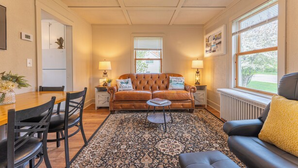 A cozy living room with a brown leather sofa, a dining table with chairs, and a patterned rug. - Camp Street Haven: 2-bedroom peaceful getaway (Ely)
