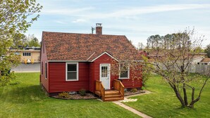 A red single-story house with a red door, a small front porch, and a sloped roof. - Camp Street Haven: 2-bedroom peaceful getaway (Ely)