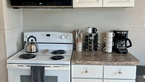 A kitchen with white cabinets, a stove, a kettle, a coffee maker, and a microwave. - Camp Street Haven: 2-bedroom peaceful getaway (Ely)