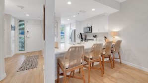 A modern kitchen with white cabinets, a central island, and a dining area with wicker chairs. - Waterfront 2BR 2BA  Pool - 10 min walk to Beach (Longboat Key)