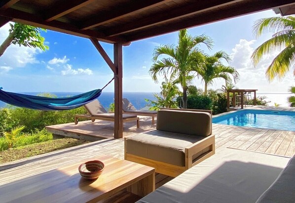 A wooden deck with a hammock, lounge chairs, and a pool.