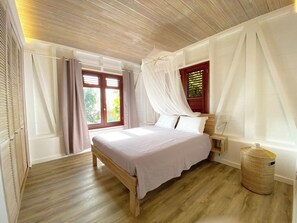 A bedroom with a wooden bed, a bedside table, a wicker basket, and a window with curtains.