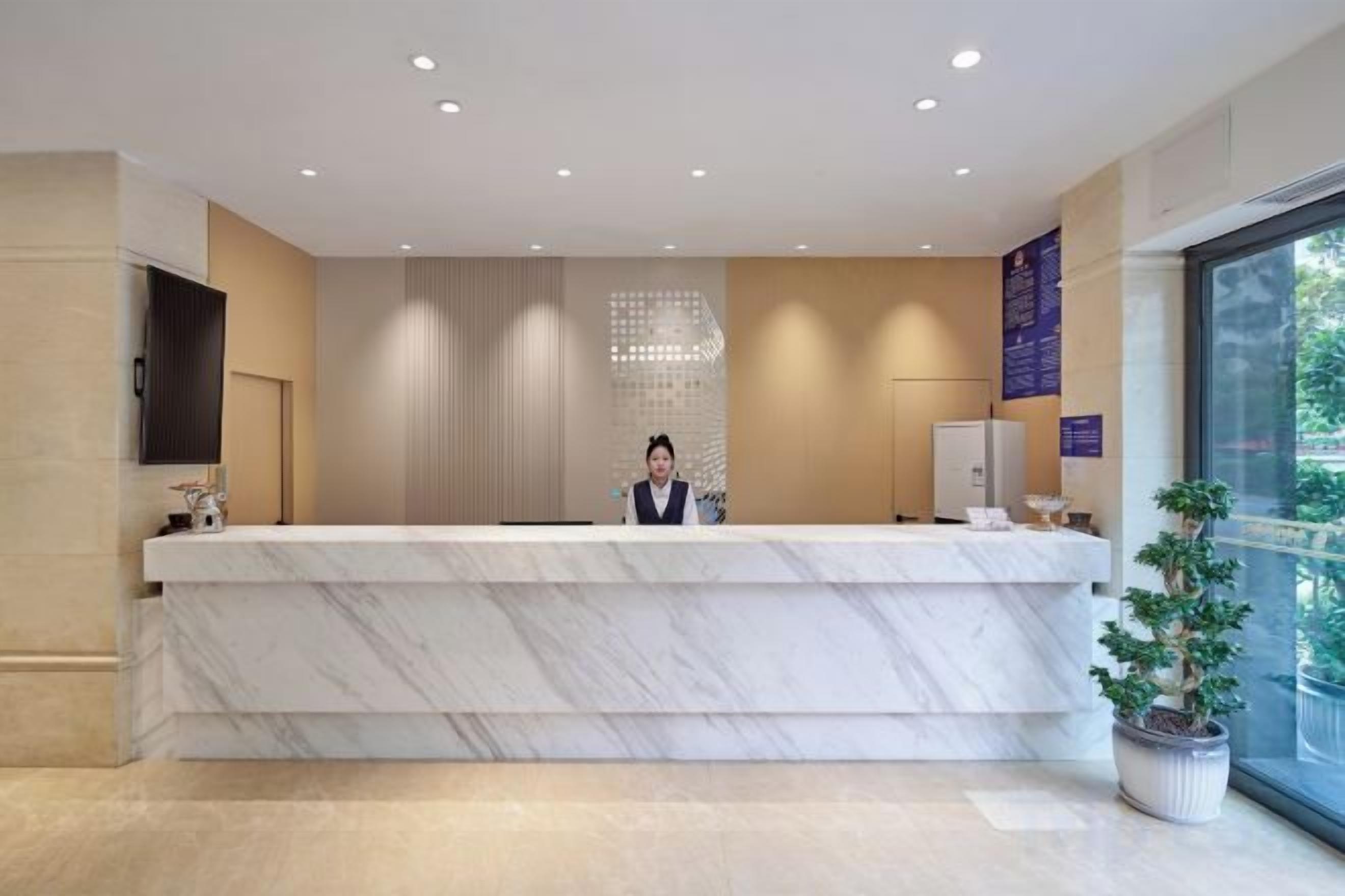 A reception desk with a marble top, a potted plant, and a large window.