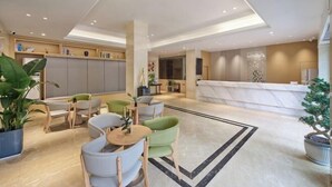 Un moderno vestíbulo de hotel con mostrador de recepción, zona de estar y una gran planta en maceta.