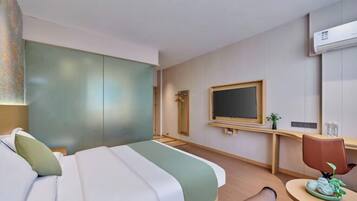 A hotel room with a bed, a desk, a chair, a television, and an air conditioning unit.