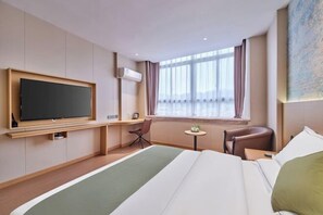 A hotel room with a large bed, a flat-screen TV mounted on the wall, a small table with a chair, and a window with curtains. - Yiju Qingyue Hotel (Xishui)