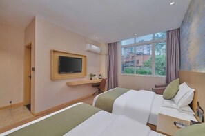A hotel room with two beds, a TV, a desk, and a window with a view of buildings and trees. - Yiju Qingyue Hotel (Xishui)