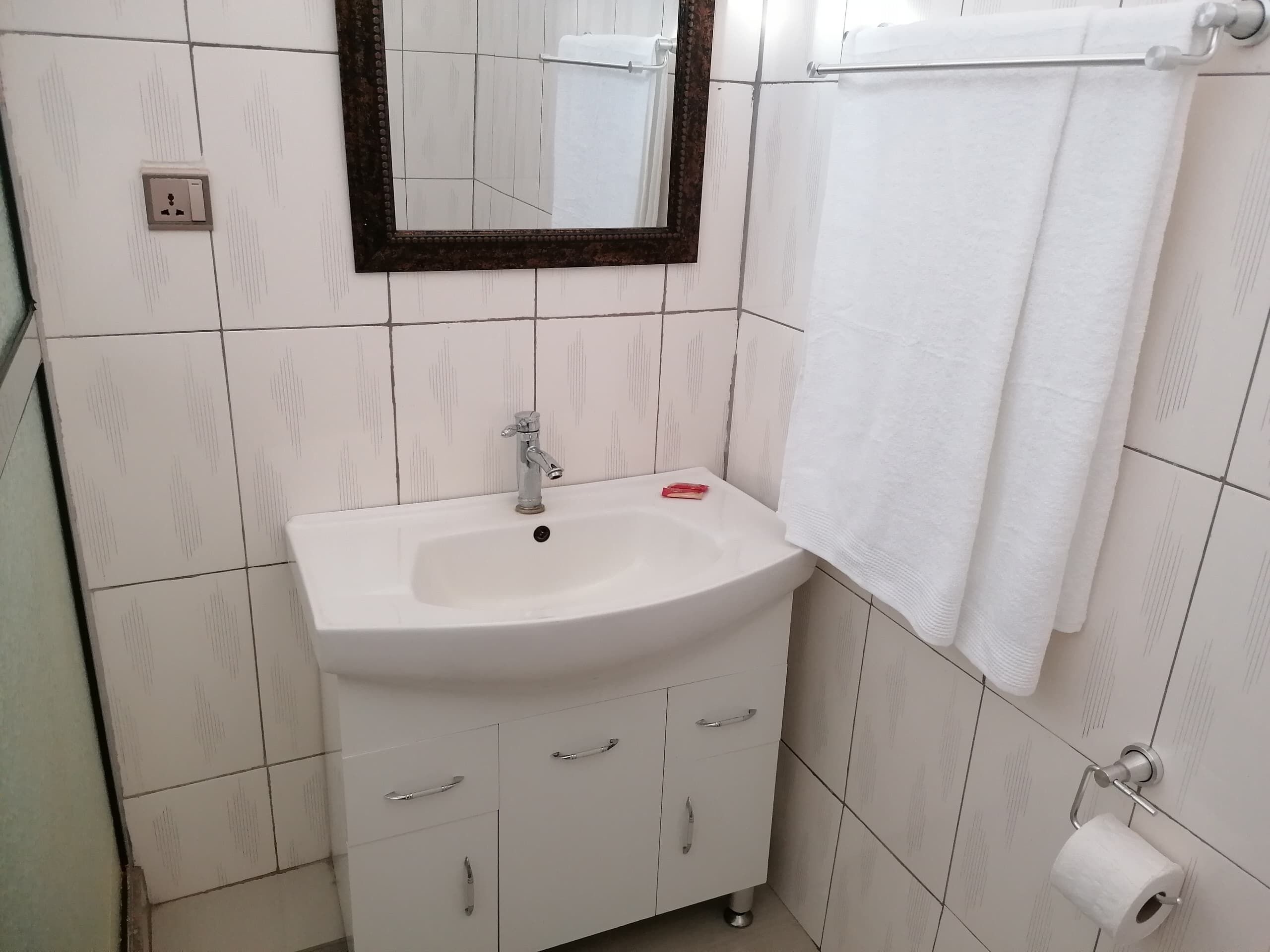 A bathroom with a white sink, a mirror, a towel rack, and a toilet paper holder.