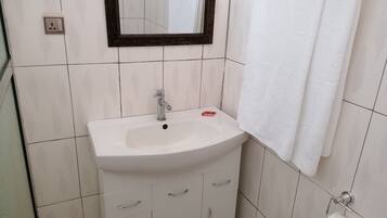 A bathroom with a white sink, a mirror, a towel rack, and a toilet paper holder.