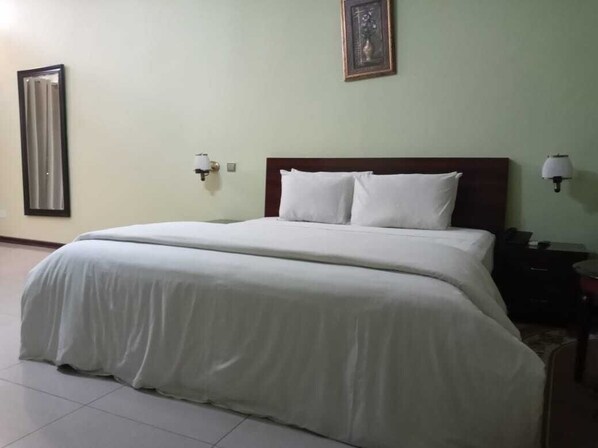 A neatly made bed with white bedding in a room with light green walls.