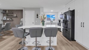 Una cocina moderna con armarios blancos, un refrigerador negro y una isla central con taburetes de bar.