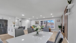 Una cocina moderna con refrigerador empotrado, armarios blancos y un comedor con mesa blanca y sillas grises.