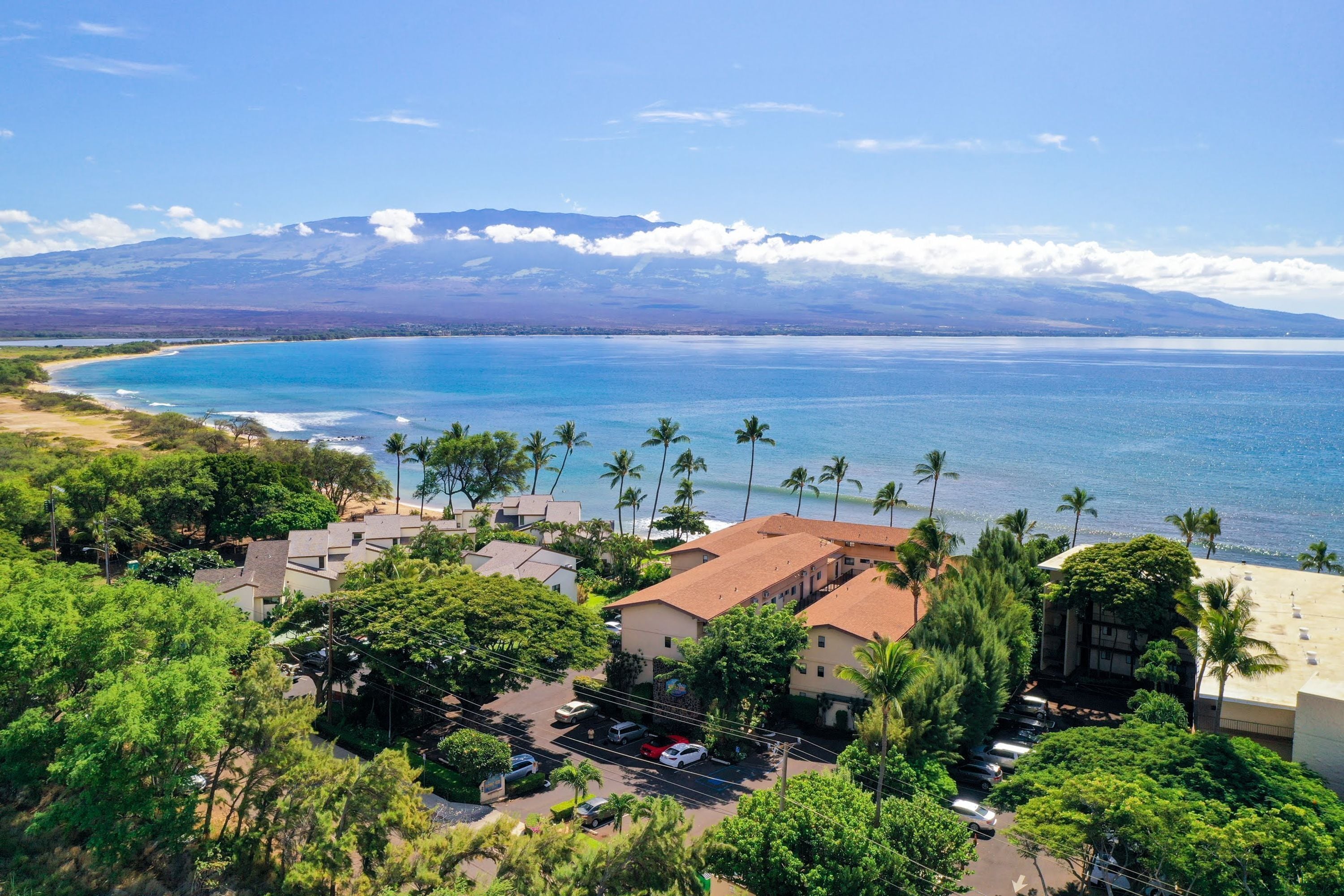 A coastal area with buildings, a parking lot, and a view of the ocean and mountains.